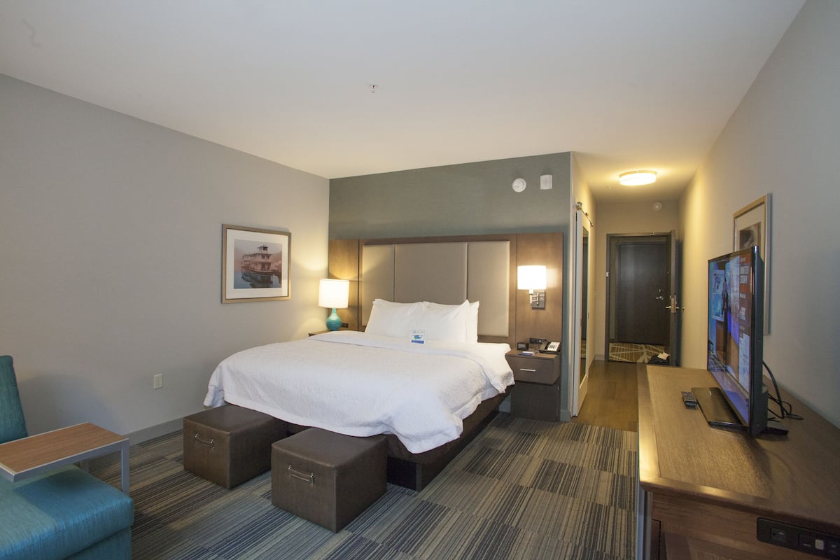 A hotel room with a bed, bedside tables, a desk, a chair, and a television.