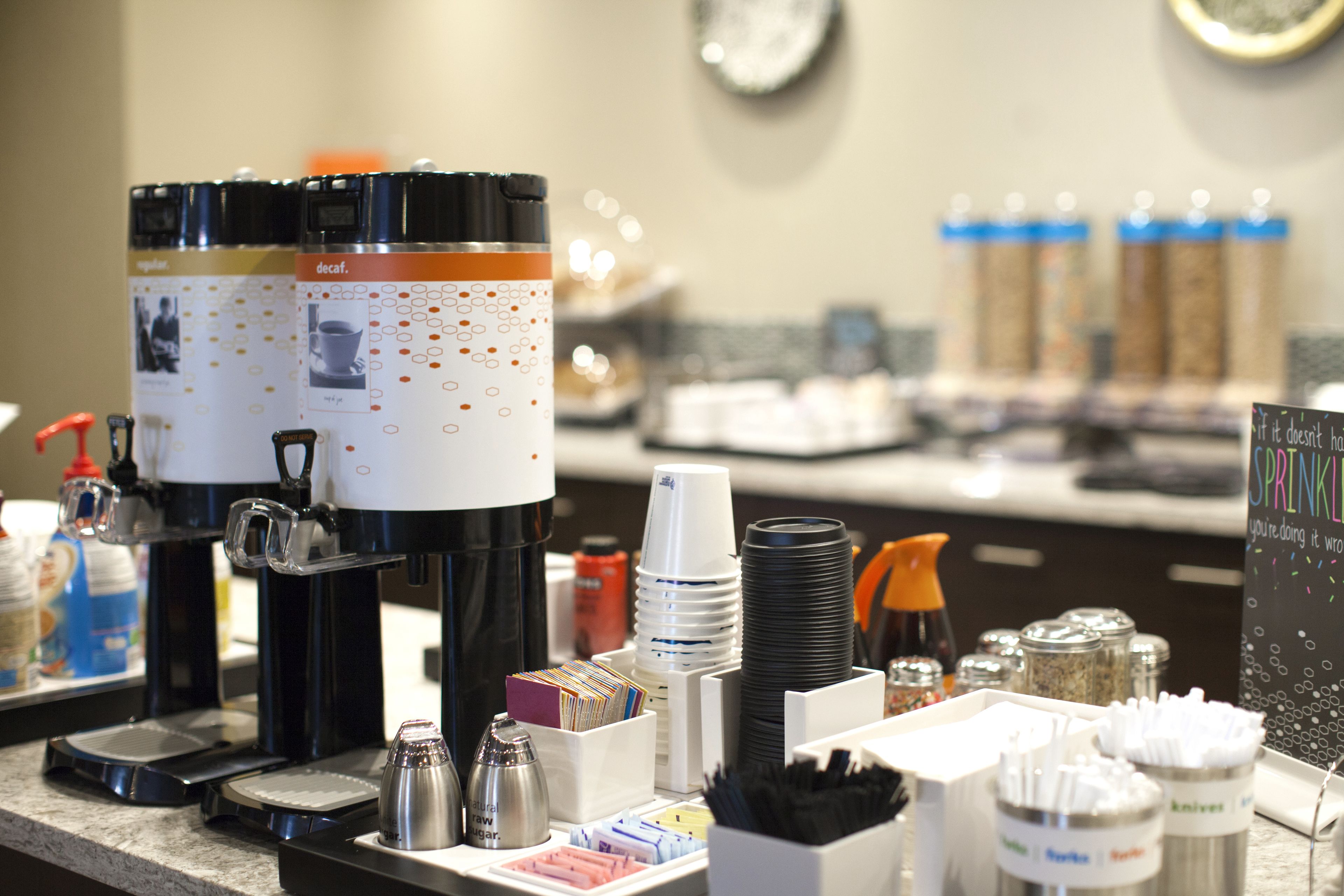 Un espace dédié au café, comprenant une machine à café décaféiné, des gobelets jetables et des condiments.