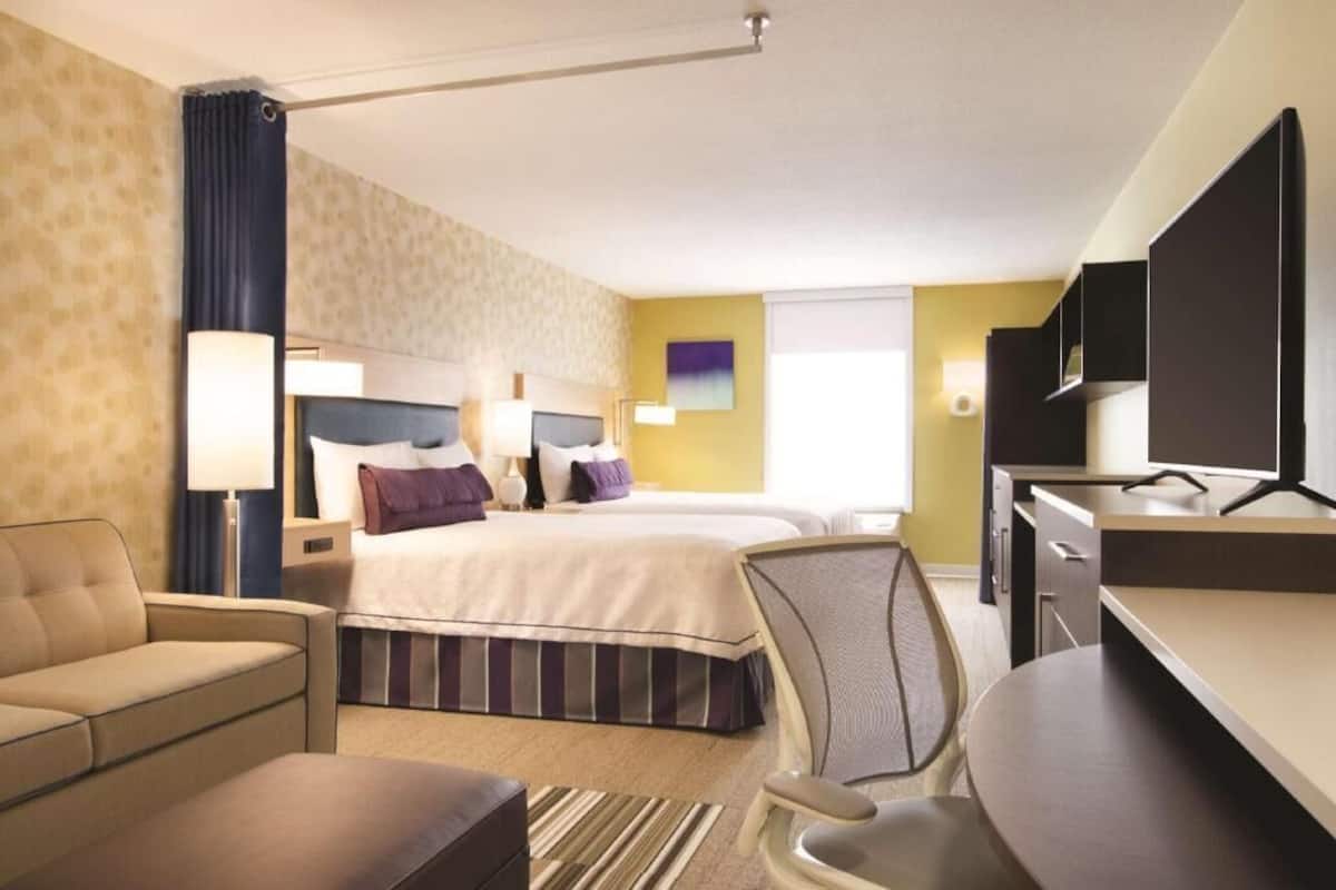 A hotel room with a bed, two bedside tables, a desk, a chair, a sofa, and a TV.