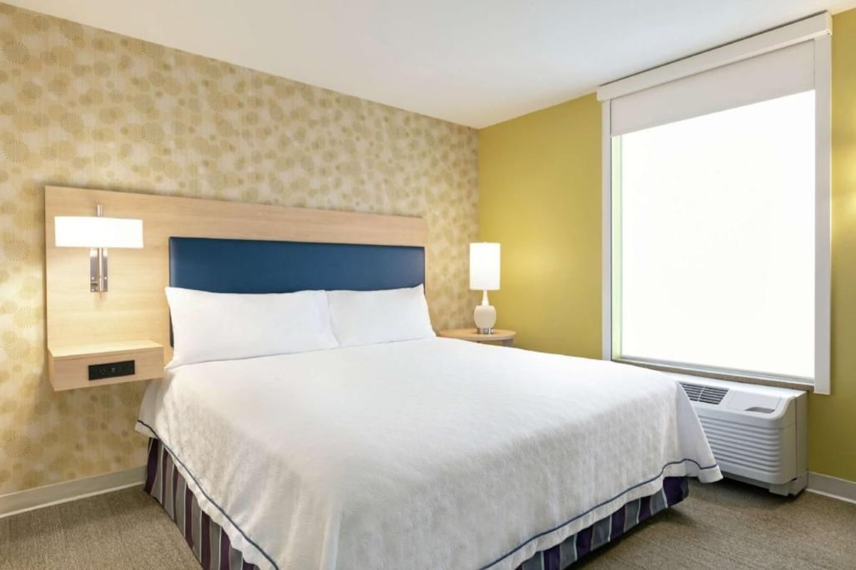 Habitación de hotel con cama, dos lámparas de noche, ventana con vistas y un calentador fijado a la pared.