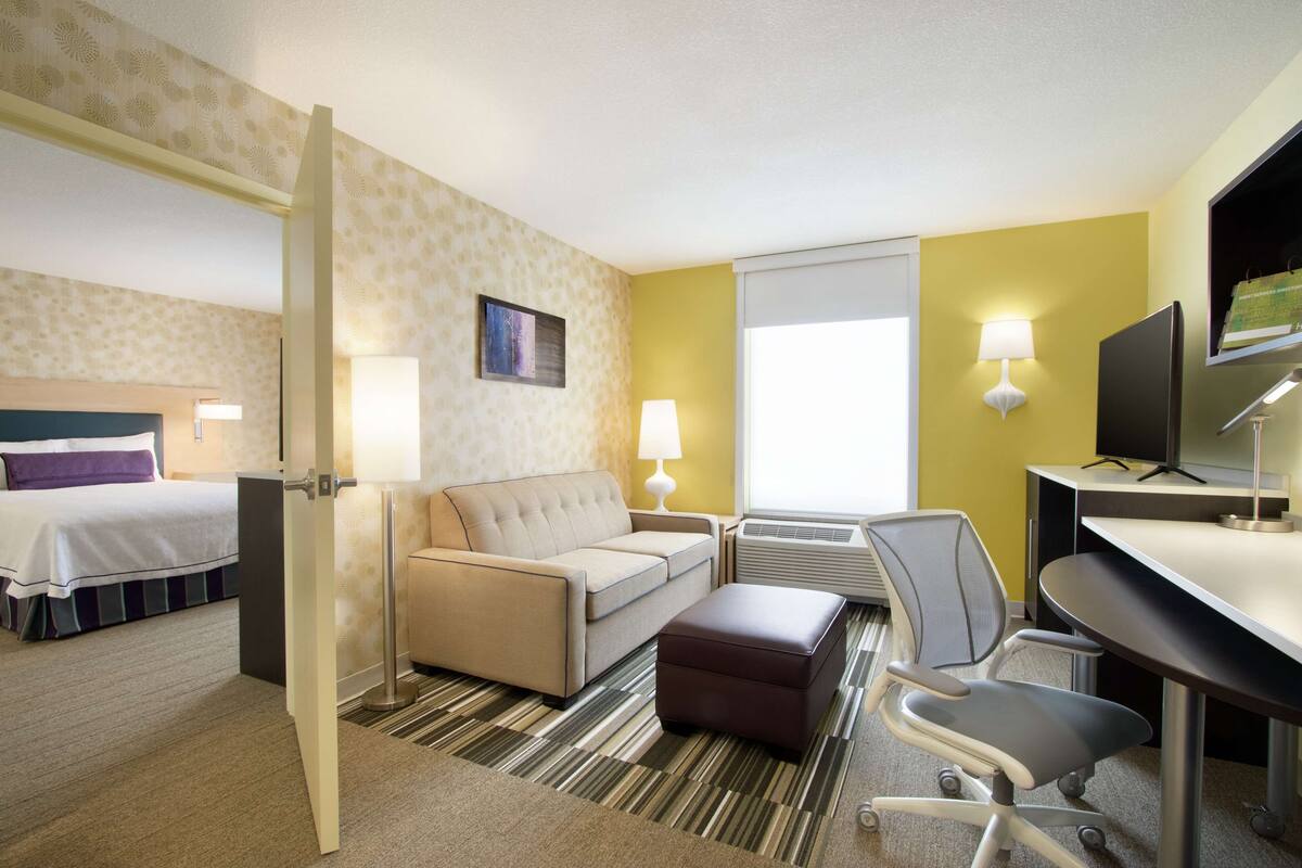 A hotel room with a bed, a sofa, a desk, a chair, and a TV.