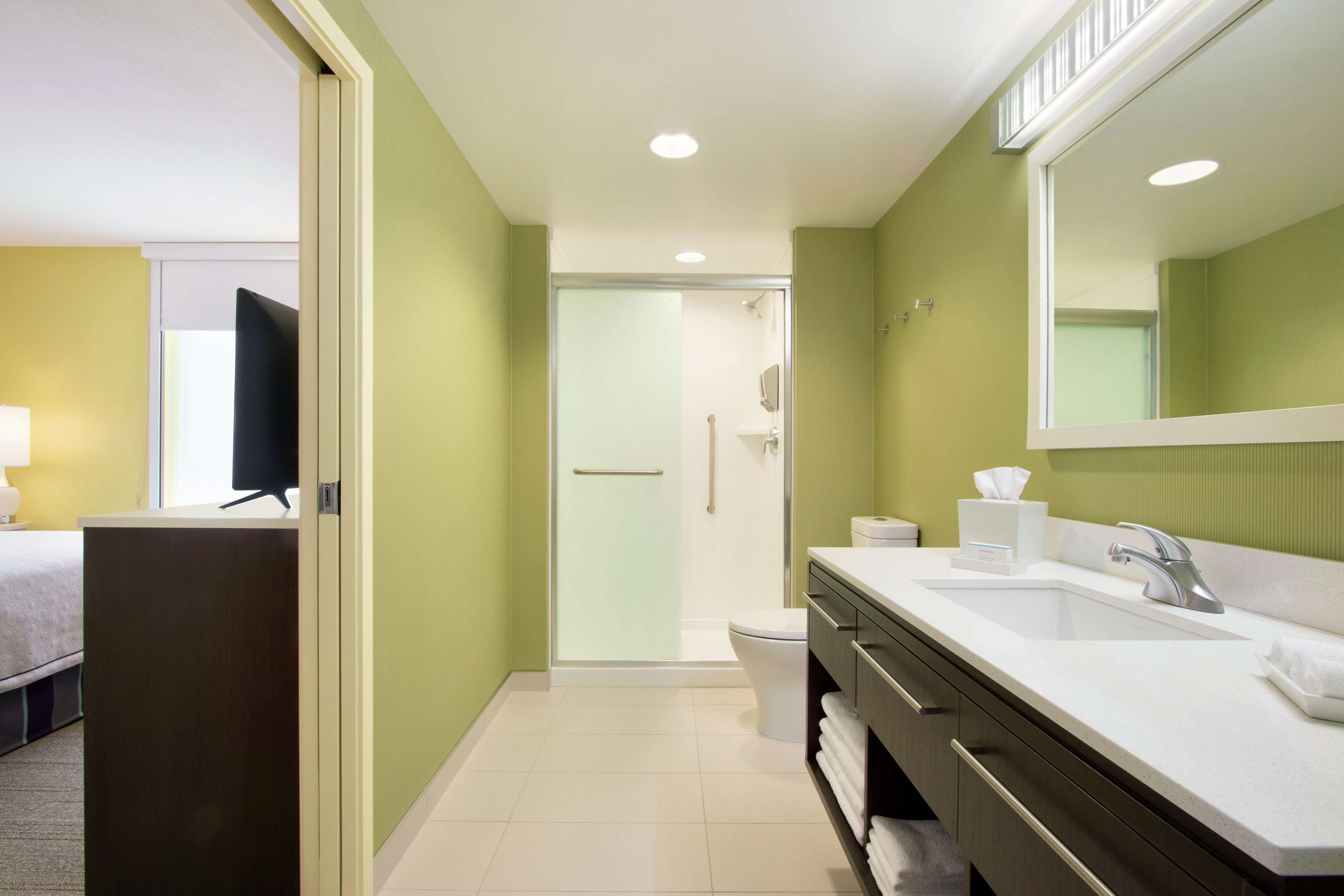 A hotel bathroom with a shower, toilet, sink, and a large mirror.