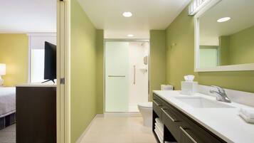 A hotel bathroom with a shower, toilet, sink, and a large mirror.