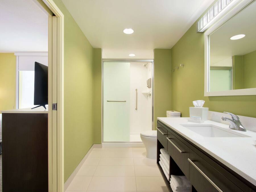 A hotel bathroom with a shower, toilet, sink, and a large mirror.