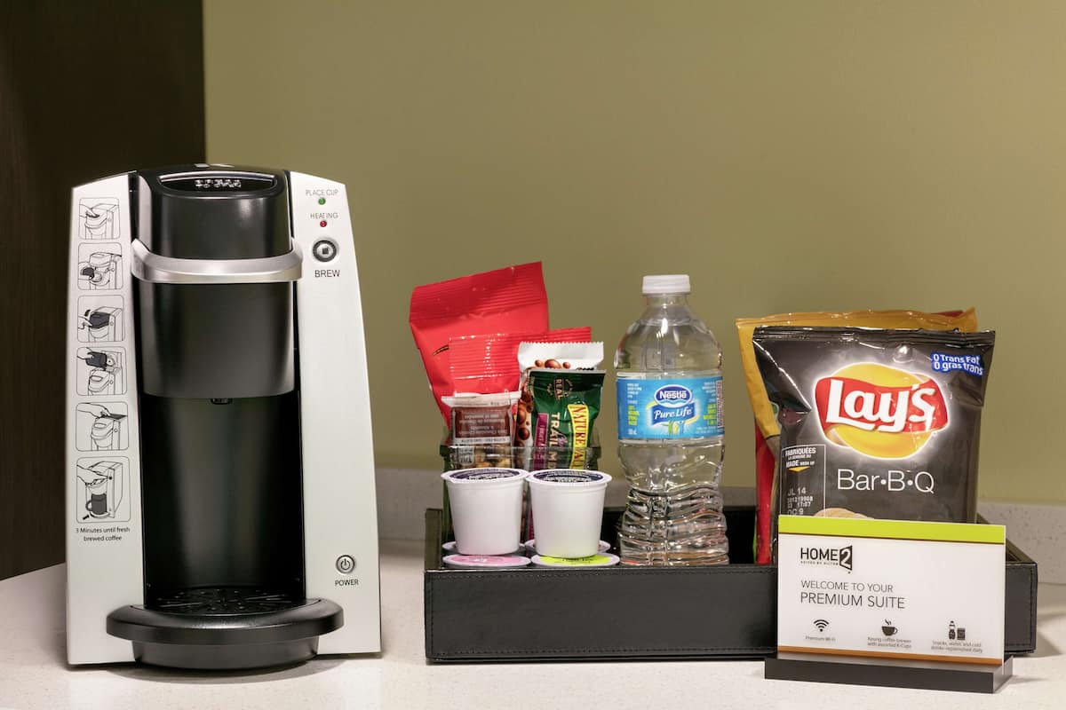 A coffee maker, a Nestle Pure Life water bottle, Lay's Bar-B-Q chips, and a welcome sign for a premium suite.