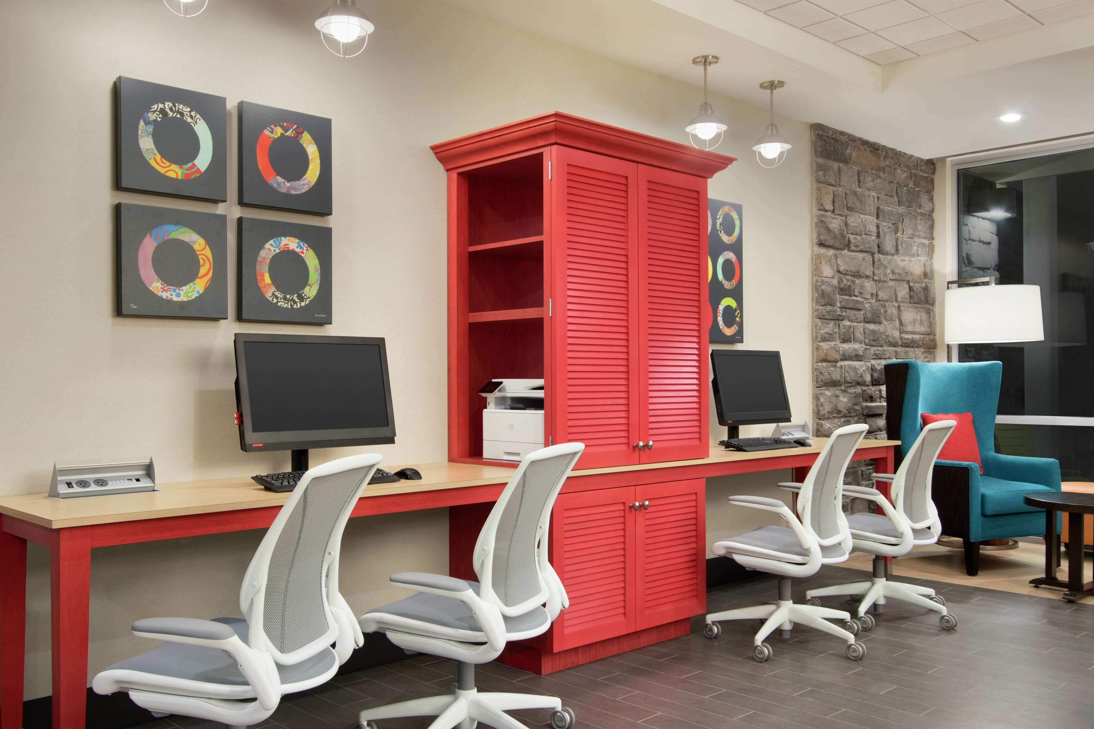 A modern office with a red cabinet, multiple monitors, and office chairs.