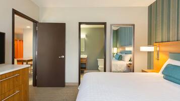 A hotel room with a bed, a dresser, a mirror, a bathroom with a toilet and sink, and a shower area.