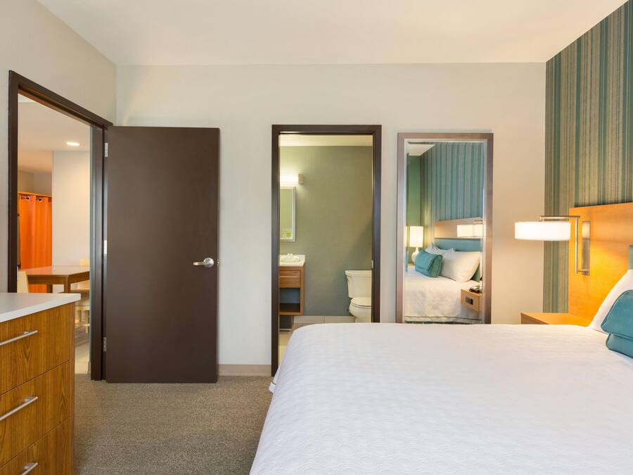 Habitació d'hotel amb un llit, una petita taula de nit, un mirall, un bany amb vàter i rentapla, i una zona de dutxa.