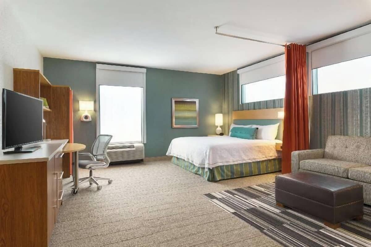 A hotel room with a bed, a desk with a computer, a chair, a sofa, and a TV.