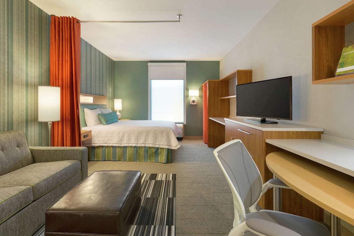 A hotel room with a bed, a desk, a TV, a sofa, and a window.