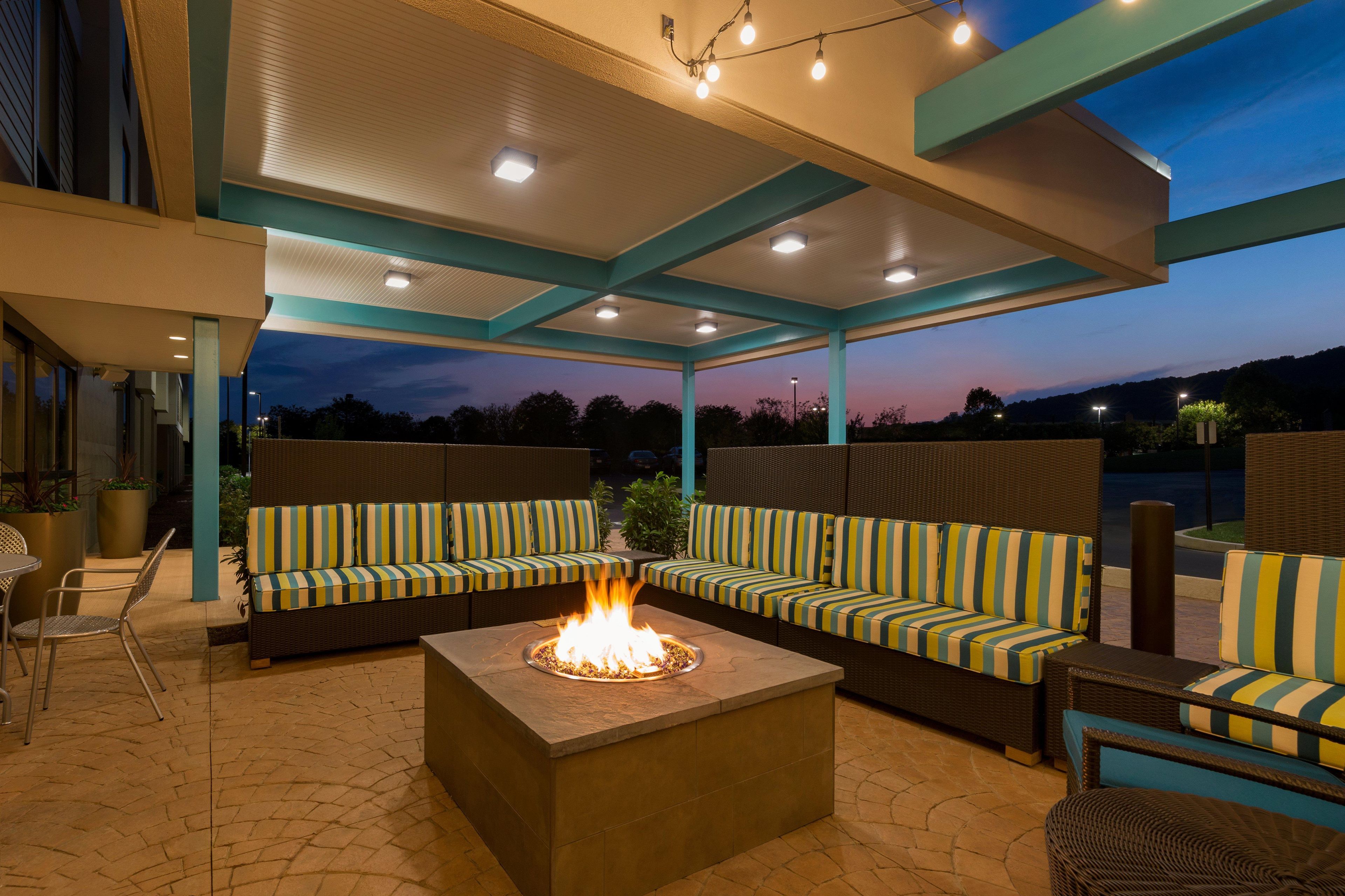 An outdoor seating area with a fire feature, covered by a roof, and a view of the sky.
