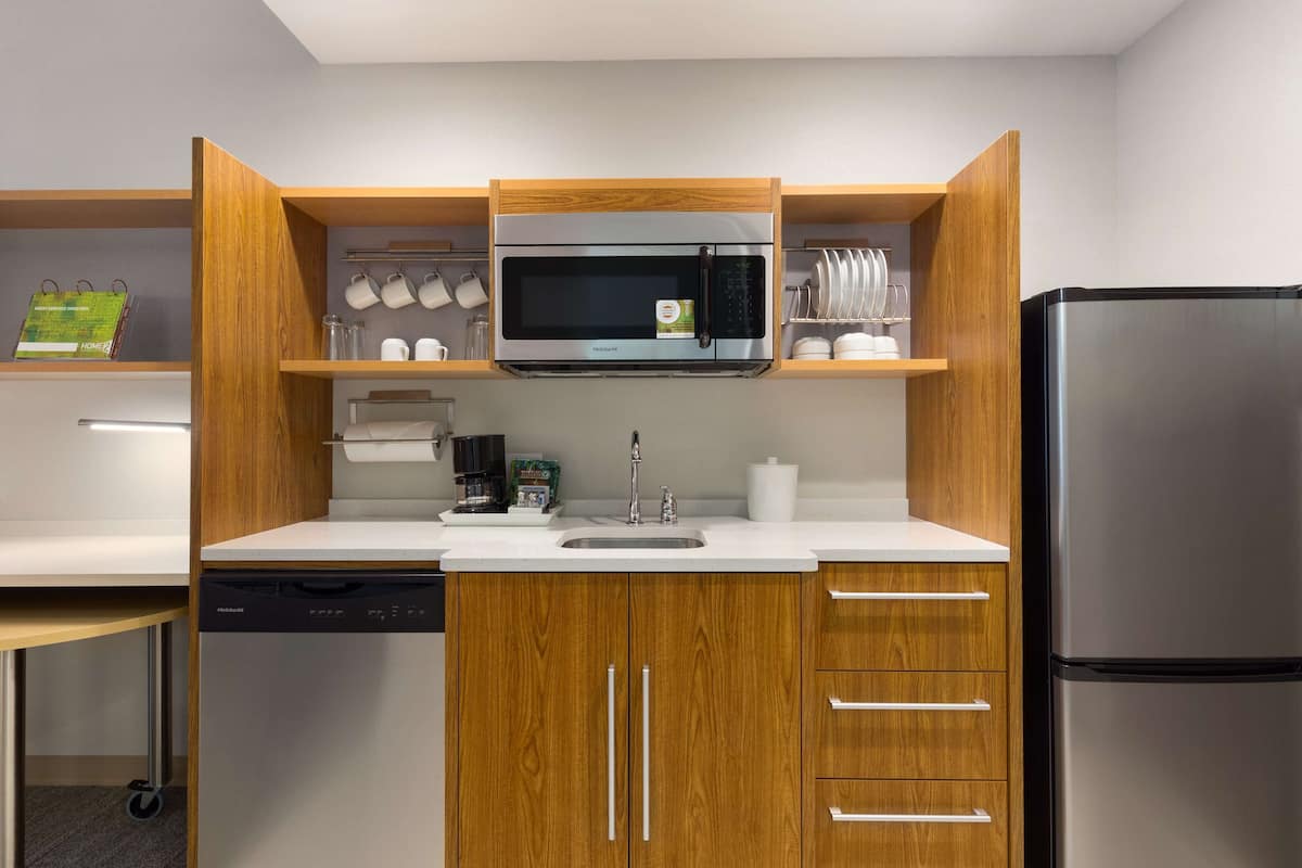 A compact kitchen with a built-in microwave, stainless steel refrigerator, and wooden cabinetry.