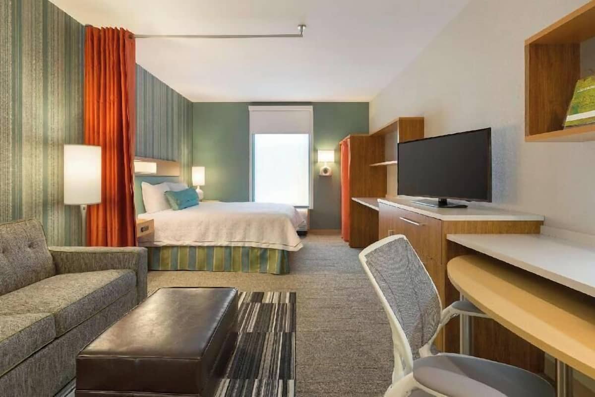 A hotel room with a bed, a desk, a chair, a television, and a sofa.
