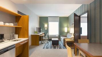 Habitación de hotel compacta con kitchenette, zona de estar con sofá y sillones, una pequeña mesa de comedor y ventana que proporciona luz natural.