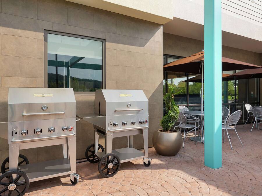 Two portable gas grills on a paved patio with outdoor seating and a building in the background.