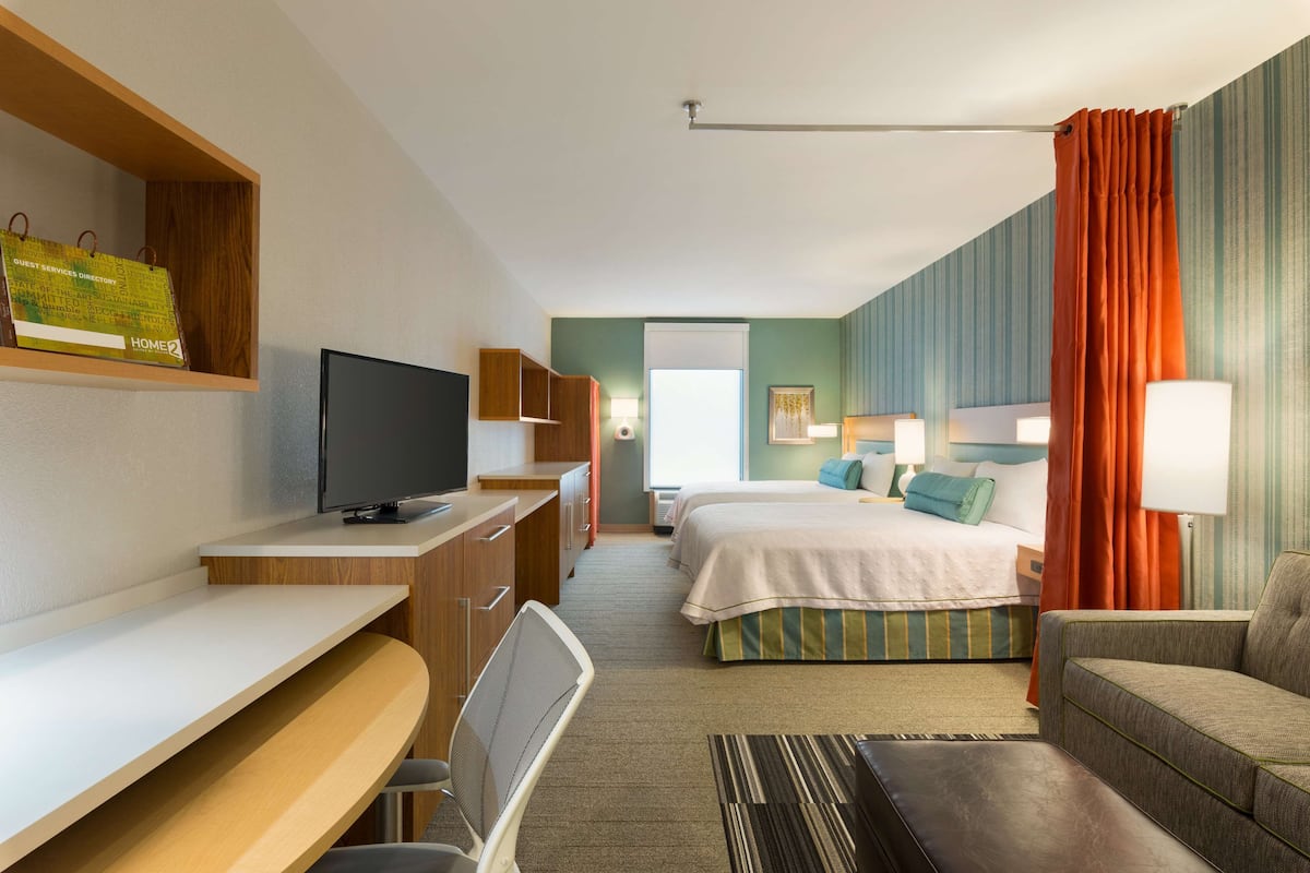 A hotel room with a desk, television, two beds, a sofa, and a bathroom visible through an open door.