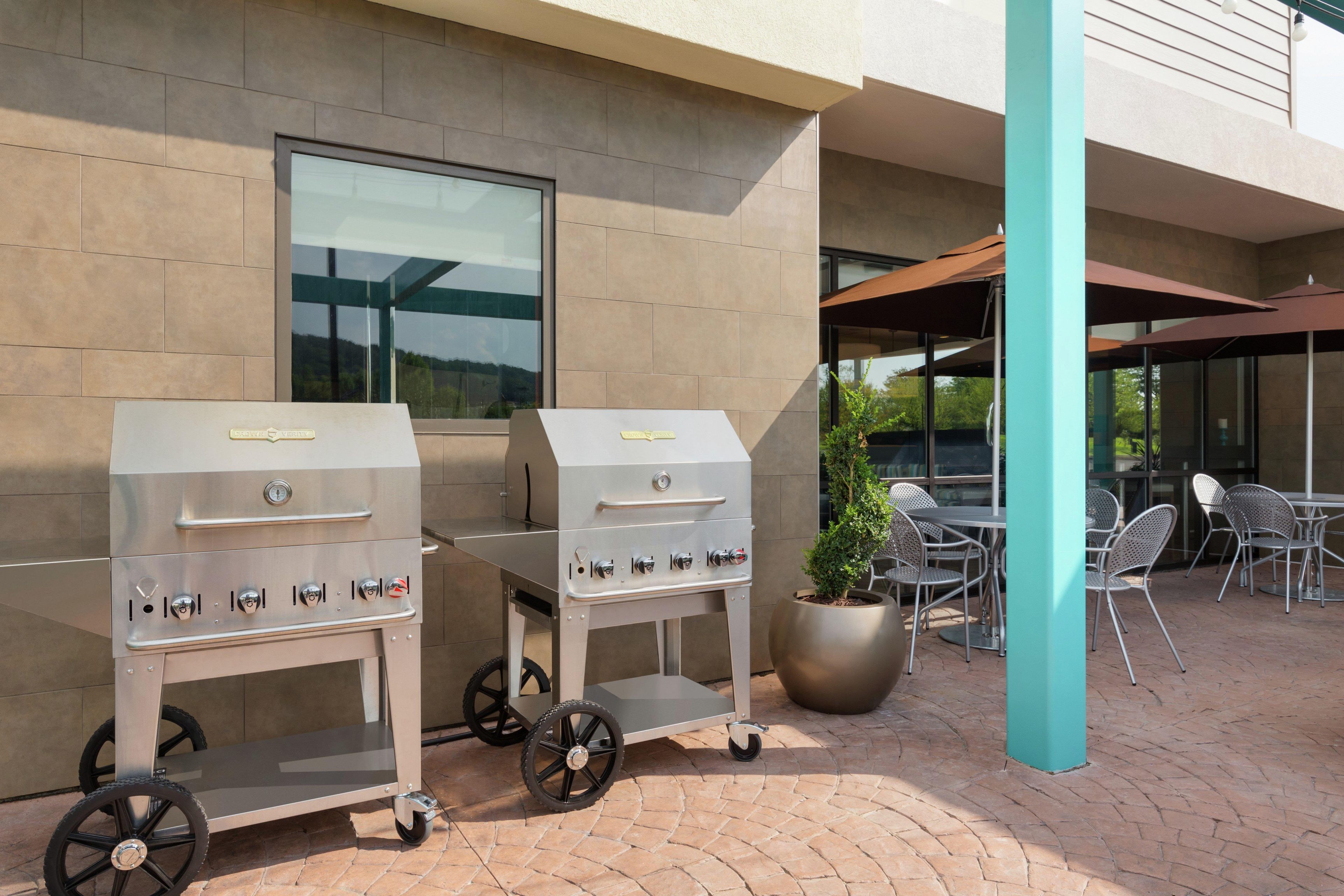 Two portable gas grills with wheels, a seating area with metal chairs, and a potted plant.