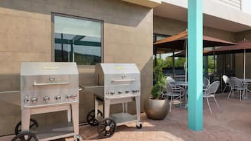 Two portable gas grills with wheels, a seating area with metal chairs, and a potted plant.