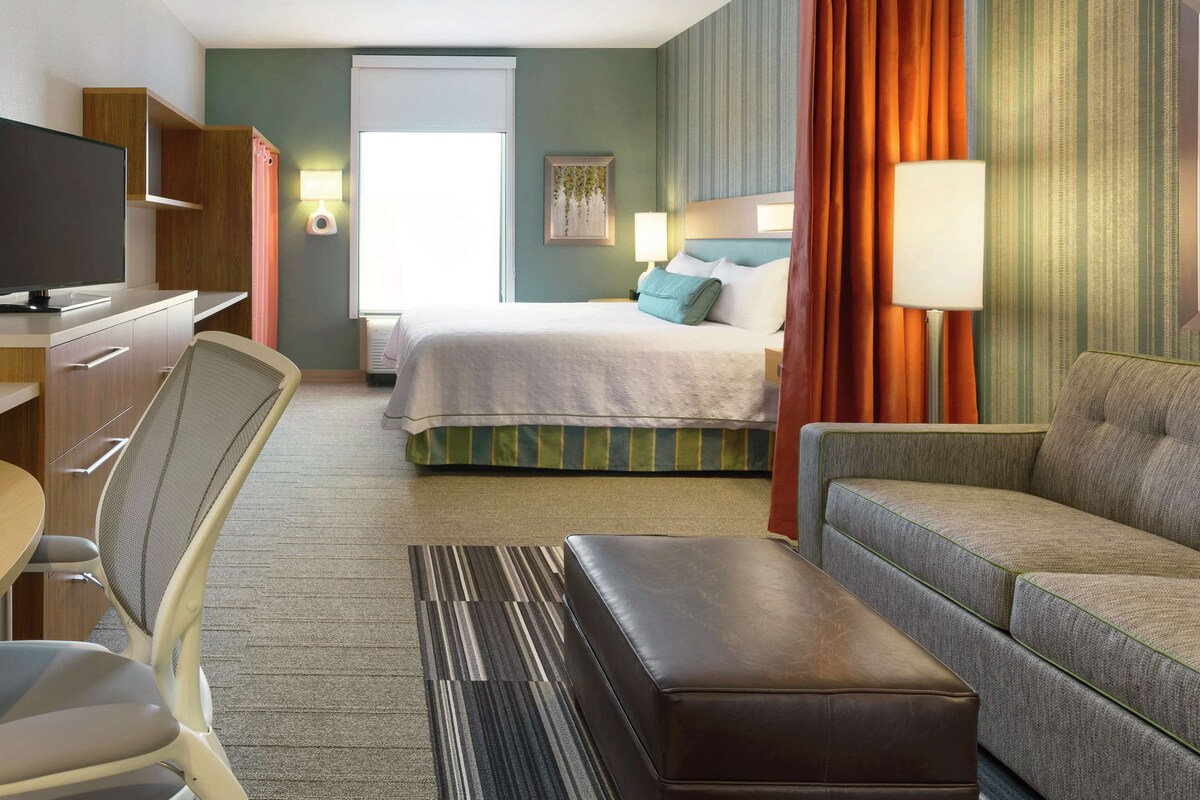 A hotel room with a bed, a sofa, a TV, a desk, and a chair.