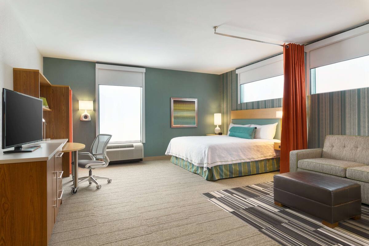 A hotel room with a bed, a desk with a computer, a chair, a sofa, and a TV.