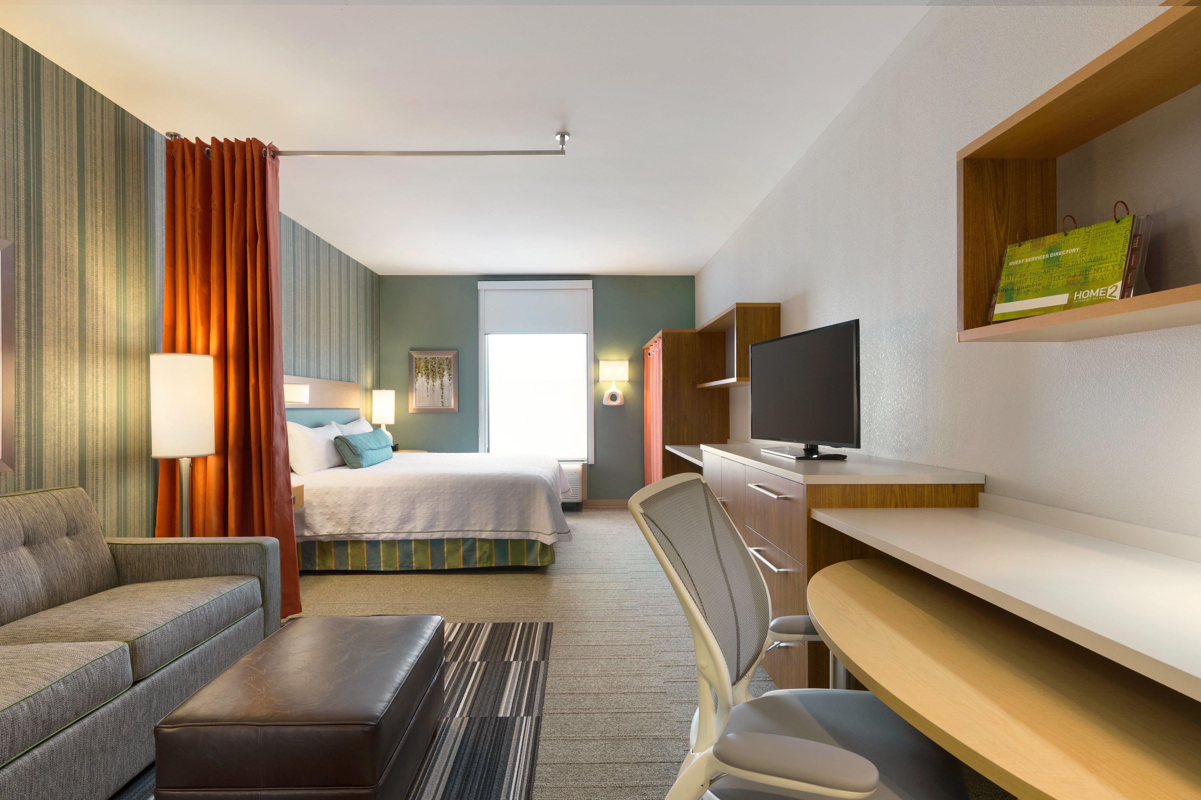A hotel room with a bed, a sofa, a desk, a TV, and a window.