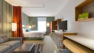 A hotel room with a bed, a sofa, a desk, a TV, and a window.