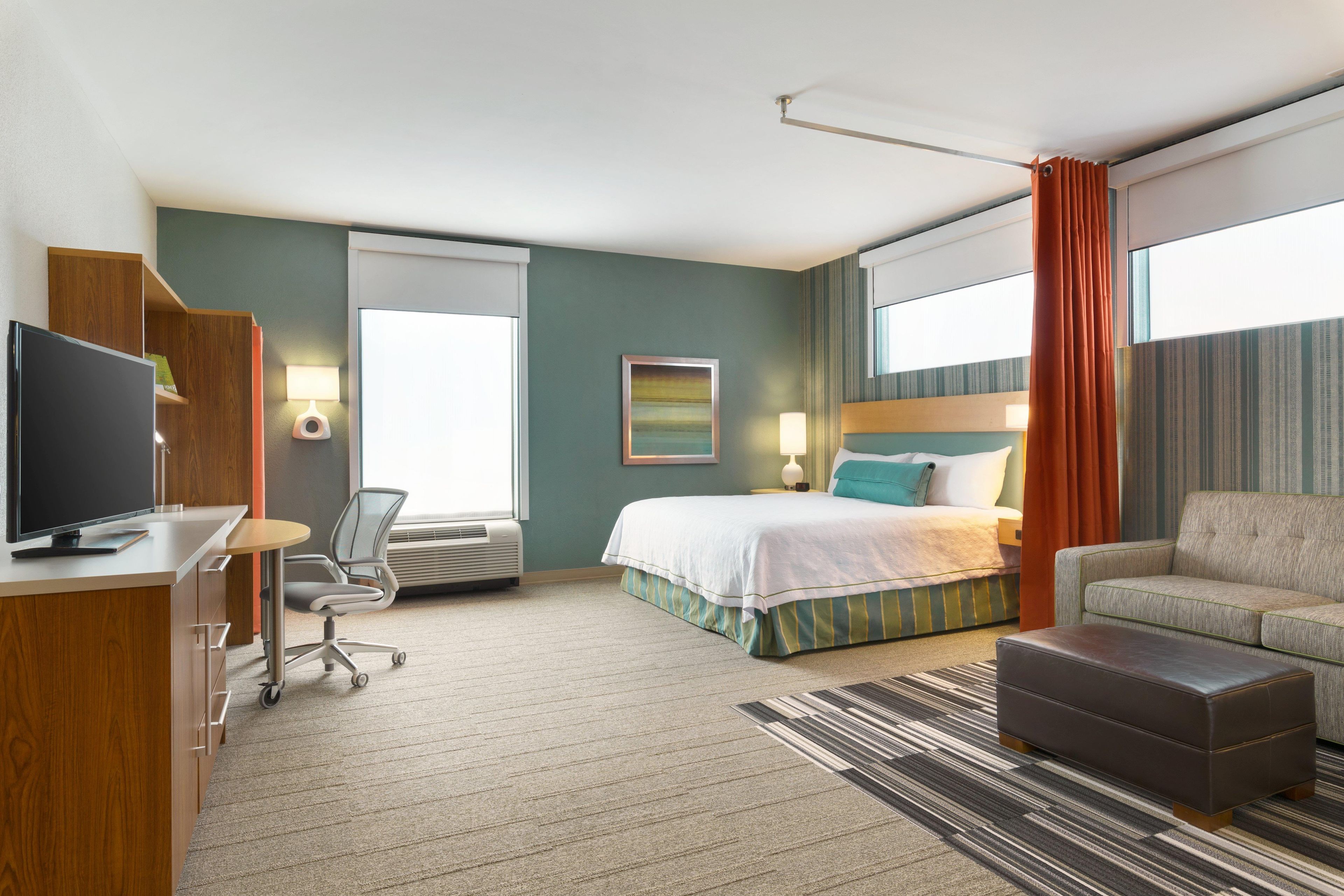 A hotel room with a bed, a desk with a computer, a chair, a sofa, and a television.