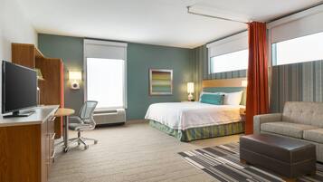A hotel room with a bed, a desk with a computer, a chair, a sofa, and a television.