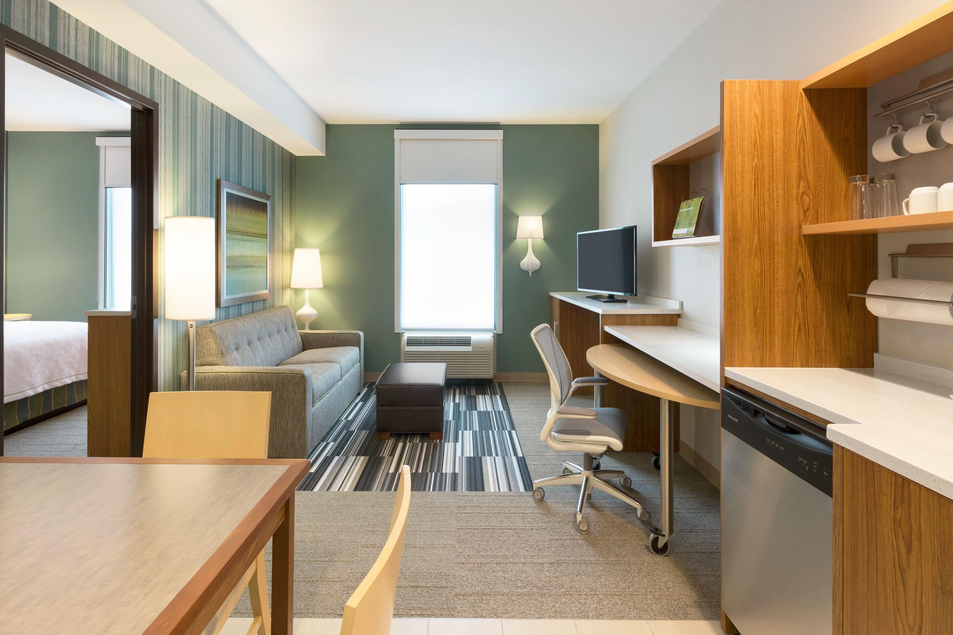 A hotel room with a bed, a sofa, a desk, a chair, a television, and a kitchenette.