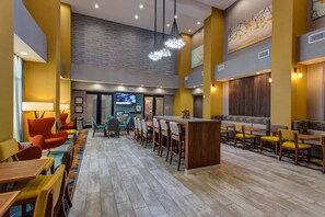 A modern hotel lobby with a long counter, multiple seating areas, and a television screen. - Hampton Inn & Suites Wichita/Airport (Wichita)