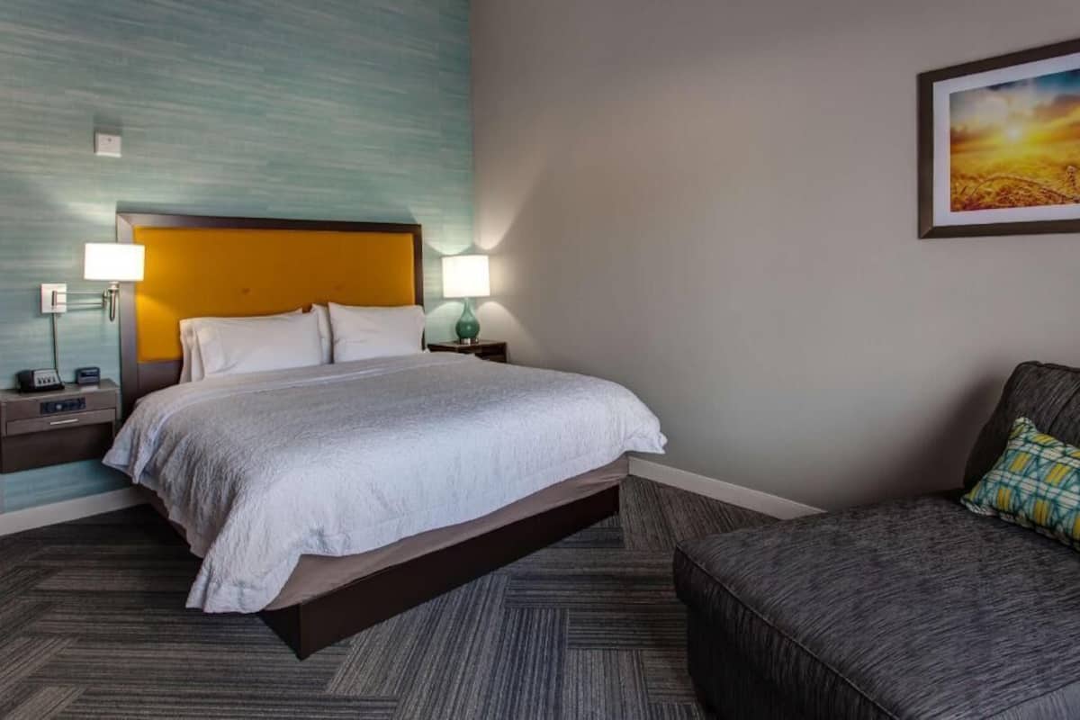 A hotel room with a bed, bedside tables, a lamp, a sofa, and a painting on the wall.