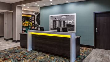 A reception desk with a yellow accent, a large framed picture on the wall, and a colorful carpet.