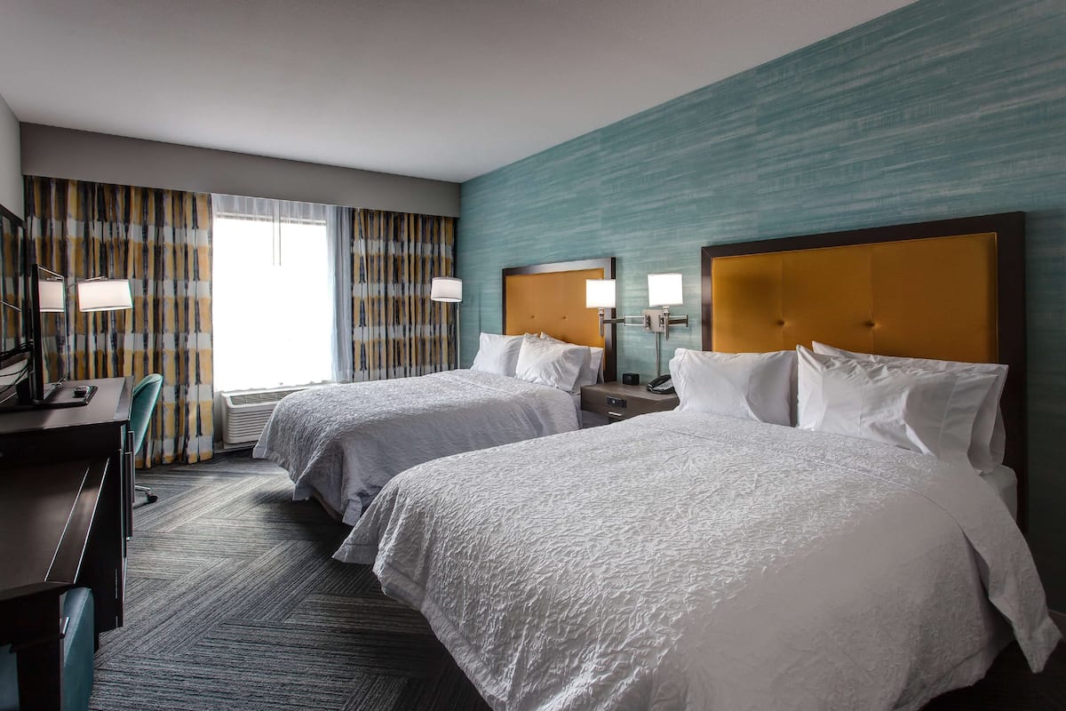 A hotel room with two beds, a desk, and a chair.