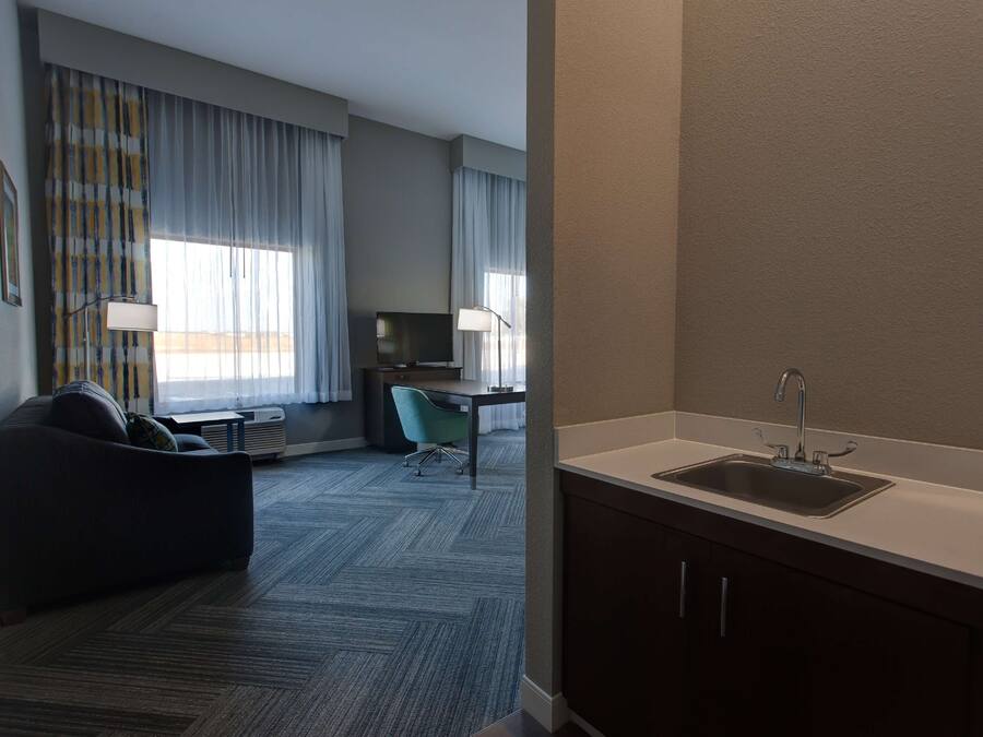 A hotel room with a kitchenette, a sofa, a desk, and a chair.