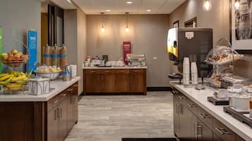 A hotel breakfast area with a buffet counter, a coffee machine, and a fruit bowl.