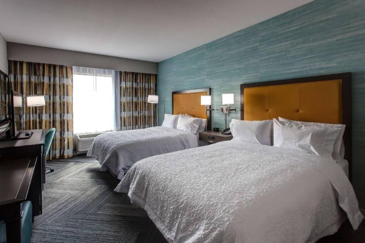 A hotel room with two beds, a desk, a chair, and a window with curtains.