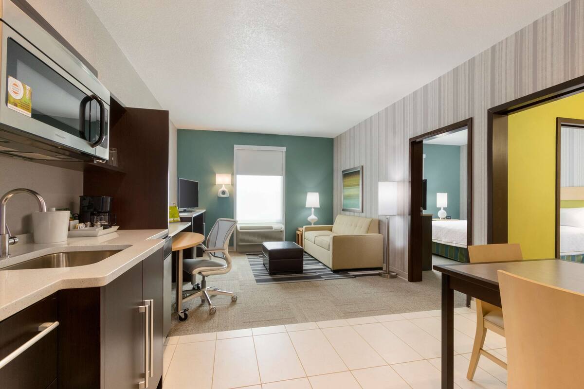 Una habitación de hotel moderna con kitchenette, un sofá, una mesa de comedor y una cama.