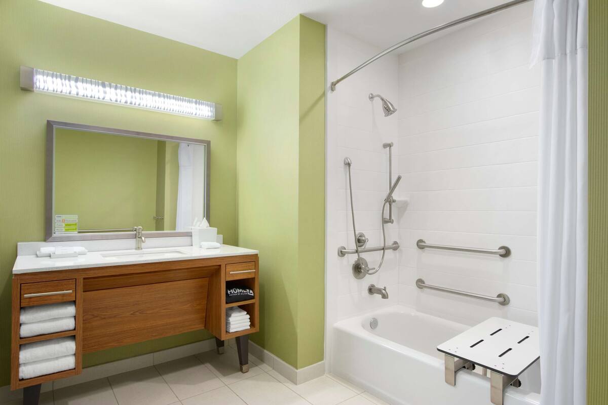Un baño con tocador de madera, un espejo grande, una bañera blanca y una ducha con barras de apoyo.