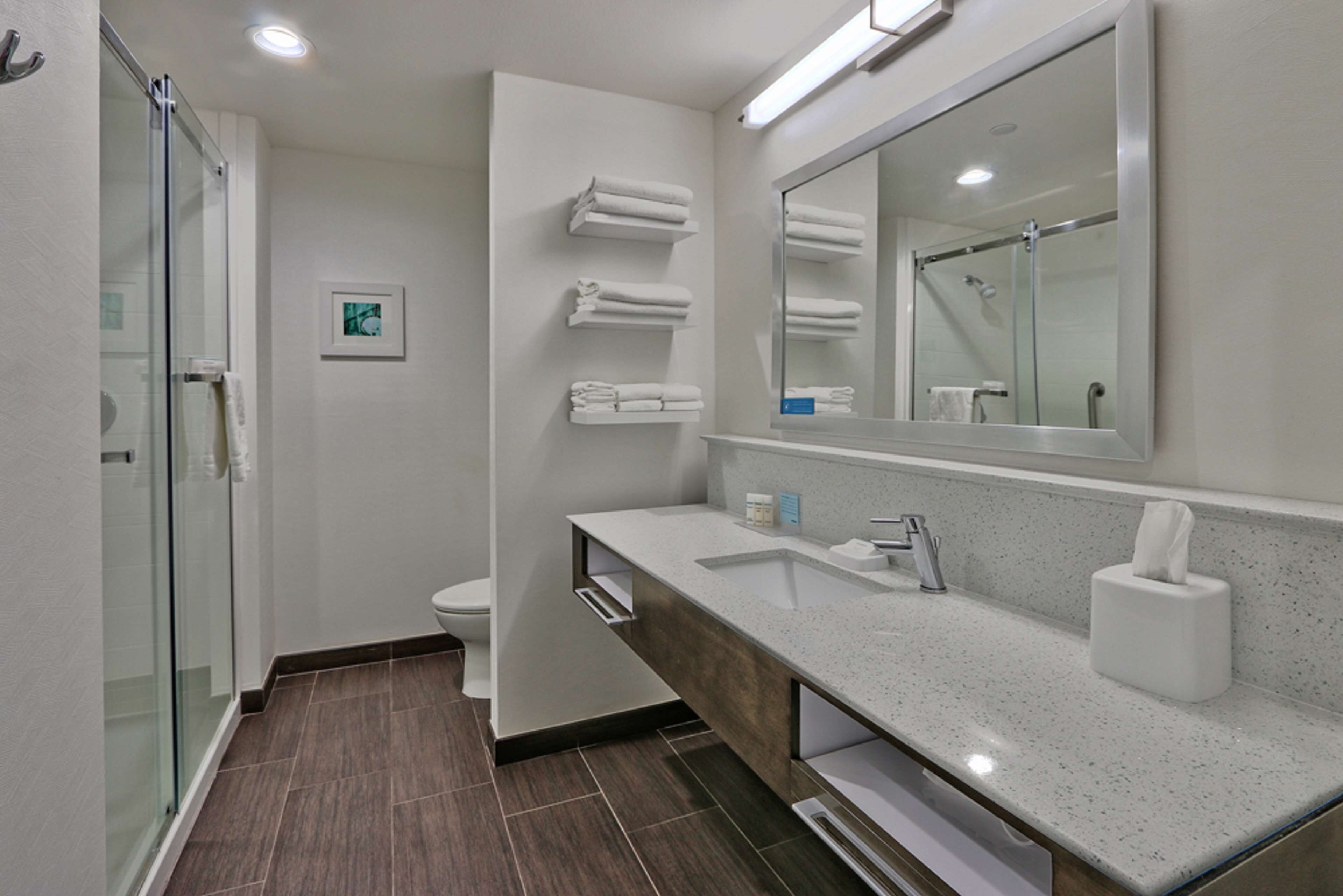 Un baño moderno con cabina de ducha de vidrio, un lavabo blanco con tocador de madera y un espejo grande sobre el lavabo.