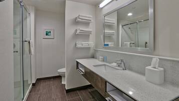 Un baño moderno con cabina de ducha de vidrio, un lavabo blanco con tocador de madera y un espejo grande sobre el lavabo.