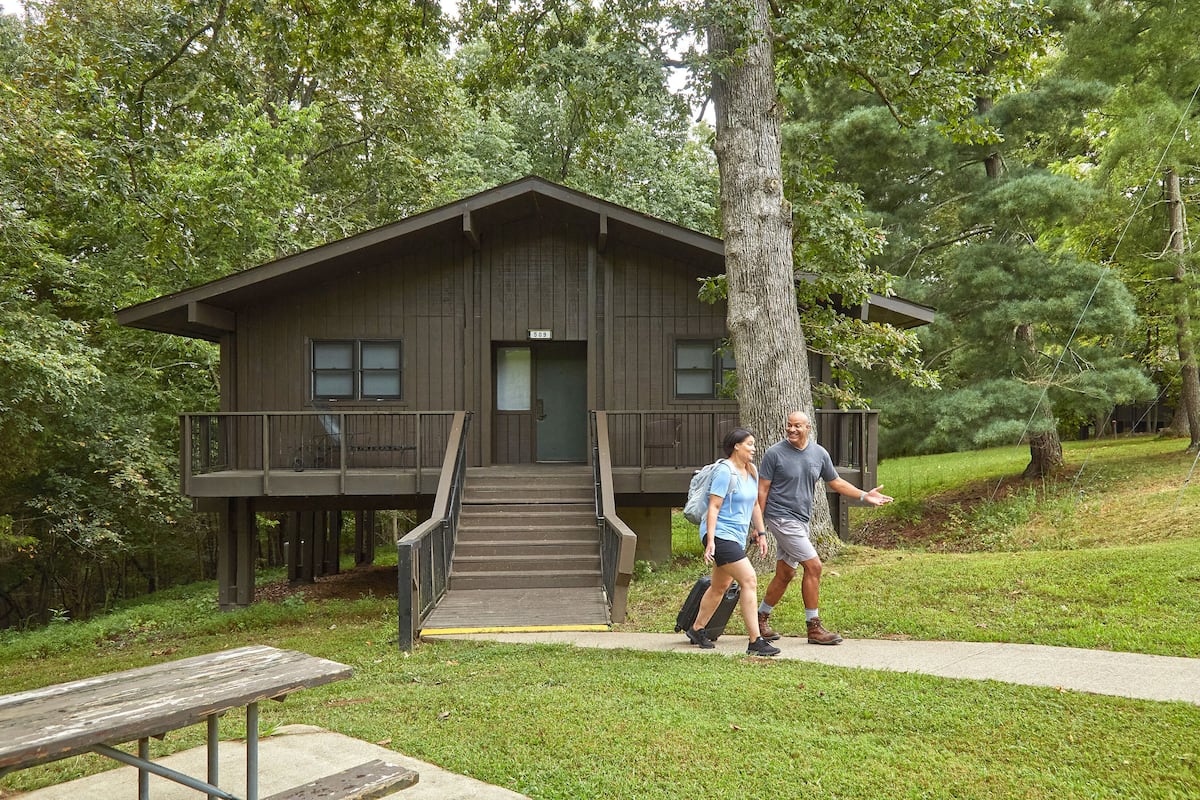 A cabin with a wooden exterior, a balcony, and a staircase leading to the entrance.