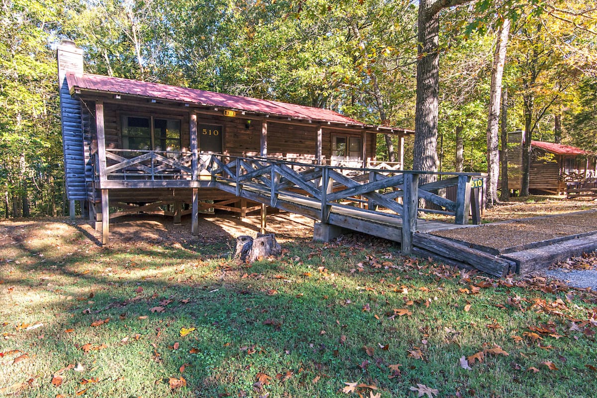 A rustic cabin with a wooden deck and a bridge leading to the entrance.