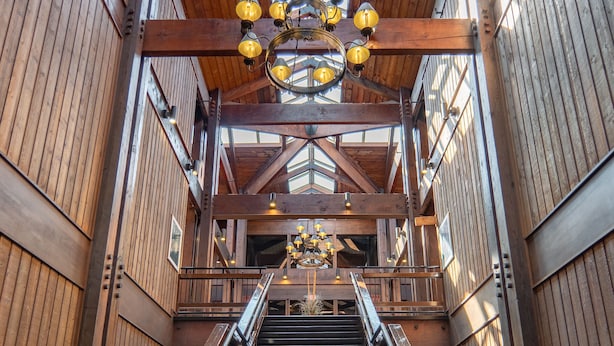 A wooden staircase with a metal railing leading to a high ceiling with a chandelier. - Lake Barkley State Resort (Cadiz)