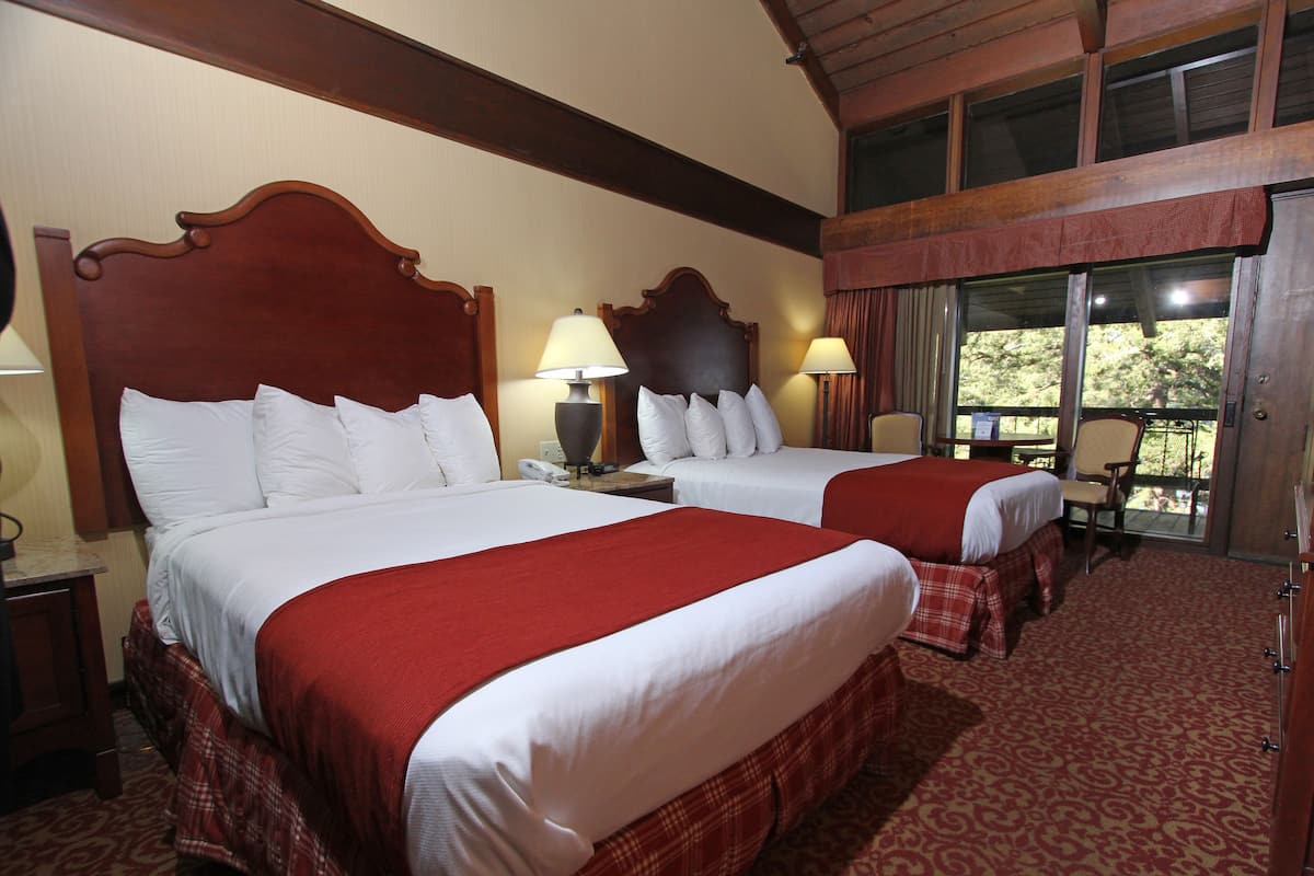 A hotel room with two beds, each with a red and white bedspread, wooden headboards, and a large window offering a view of the outdoors.