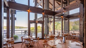 A spacious dining area with large windows overlooking a body of water, wooden tables and chairs, and a view of the landscape. - Lake Barkley State Resort (Cadiz)