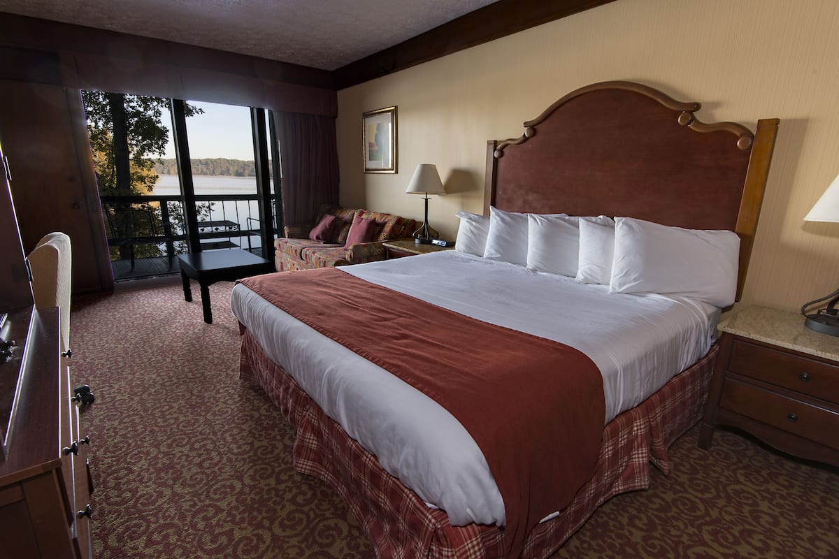 A hotel room with a large bed, a desk, a chair, and a view of a lake.
