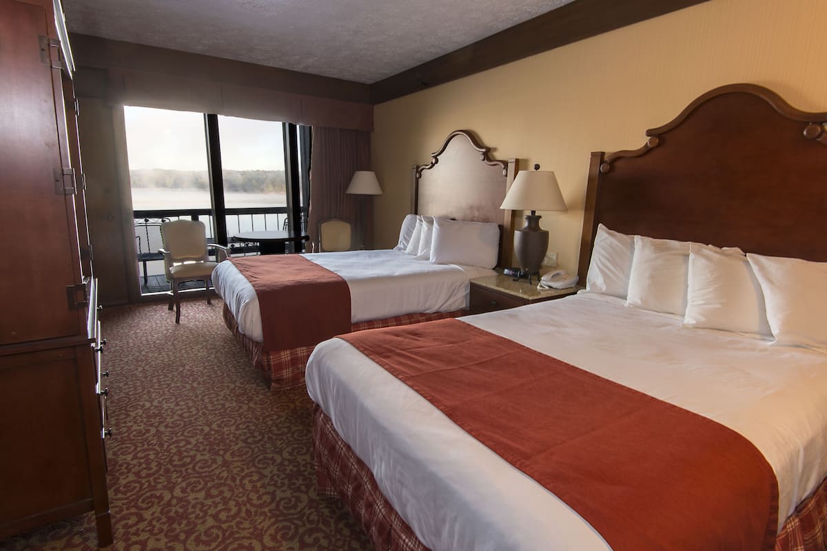 A hotel room with two beds, a desk, a chair, and a view of a lake.