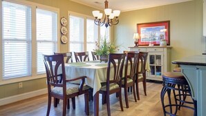 A dining room with a table set for six, surrounded by wooden chairs. There is a chandelier above the table and a cabinet with a lamp to the right. - Holden Haven 4 Bedroom Home by RedAwning (Supply)