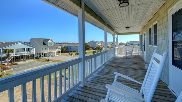 A covered porch with white railings and benches, overlooking a residential area with houses and a clear sky. - Holden Haven 4 Bedroom Home by RedAwning (Supply)