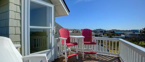 Een balkon met twee rode Adirondack-stoelen en een witte stoel, met uitzicht op een woonwijk.